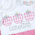 Girl's Plaid Filled Apple Trio Embroidery Design: Three pink plaid apples with bows above the name caroline in gray script on a white shirt