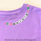Friendship Embroidery Font: Friendship bracelet style beaded letters spelling Maisie around the collar of a purple shirt