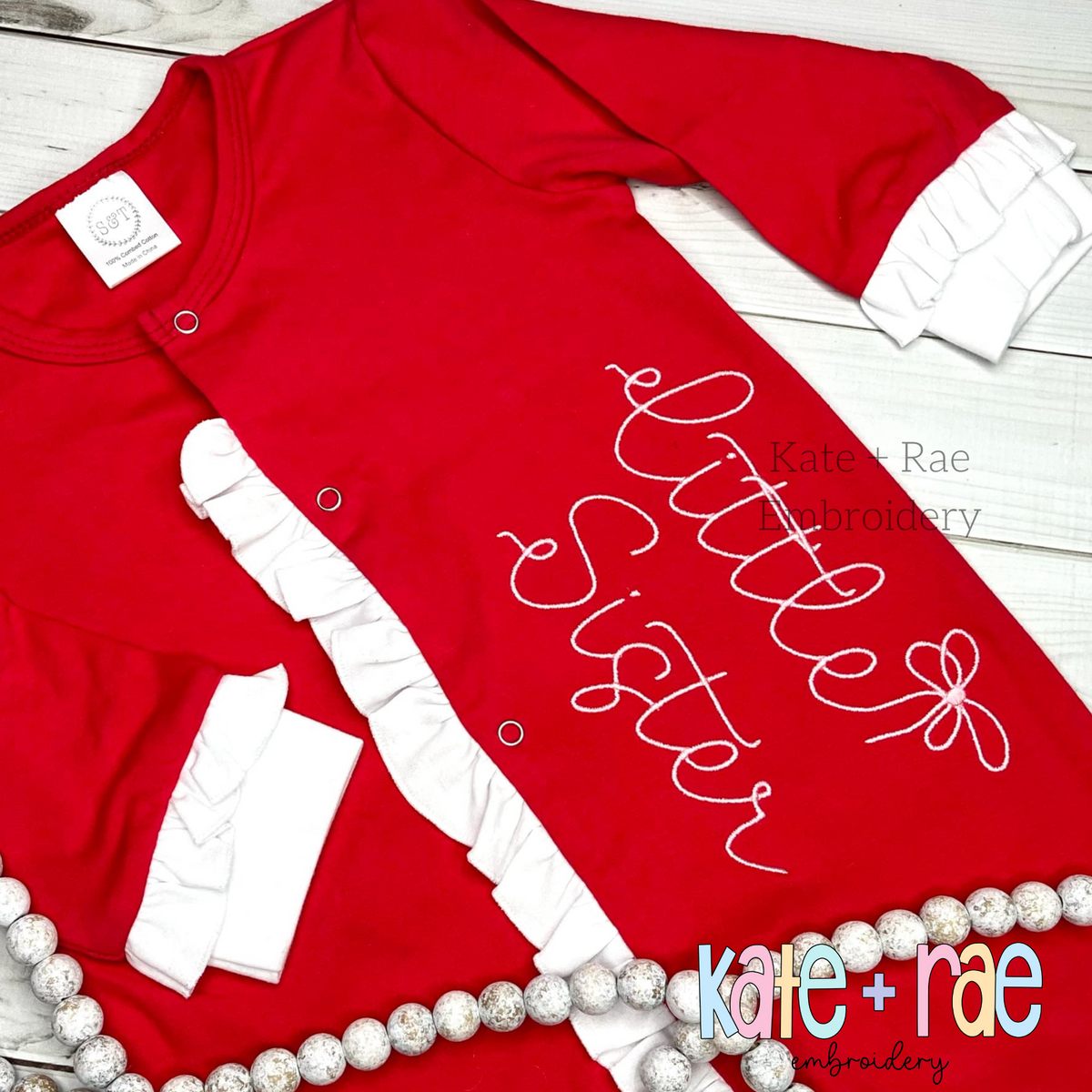 Preppy Little Sister Embroidery Design: The words little sister in white script with a bow on a red ruffled baby gown