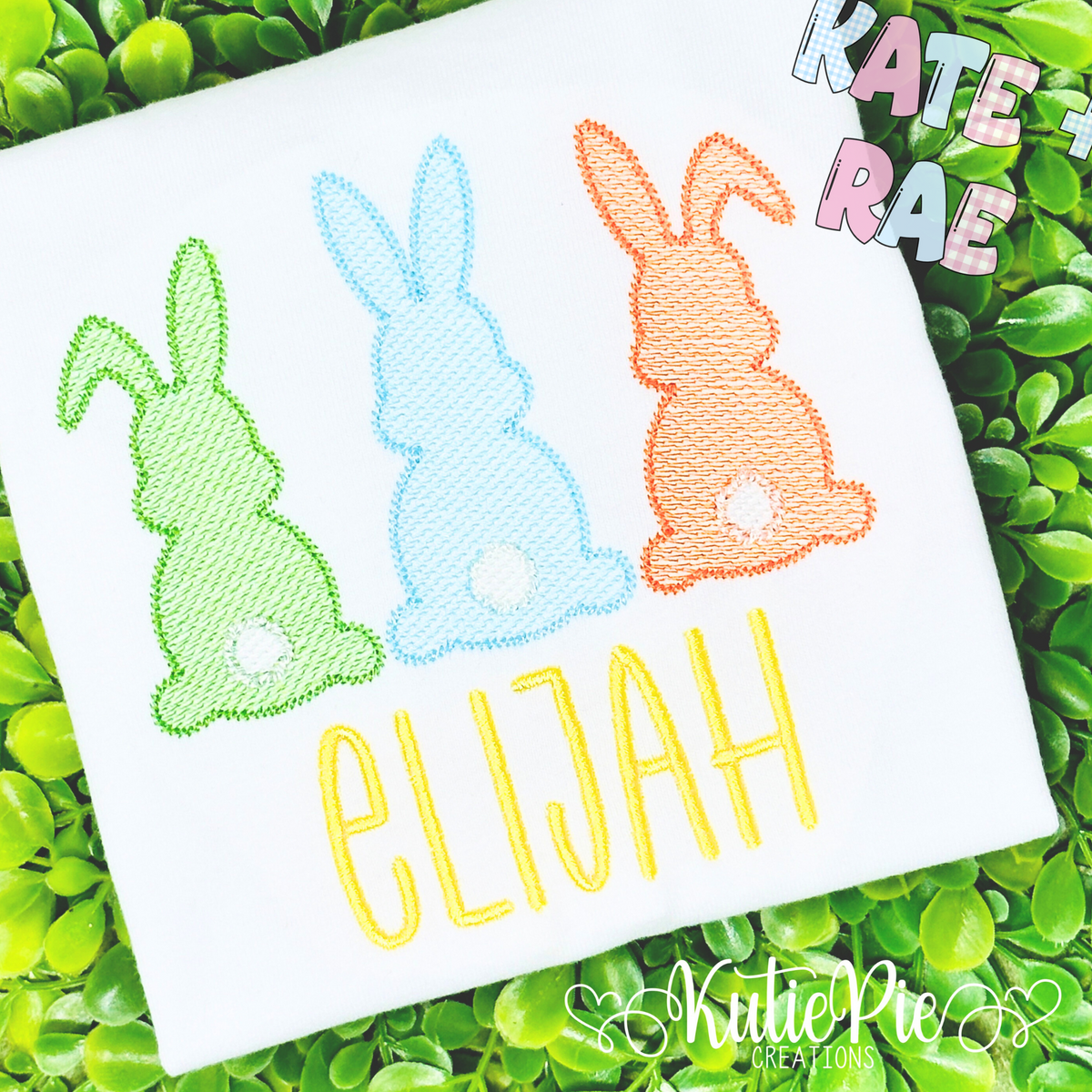 Boy's Easter Bunny Trio Sketch Stitch Embroidery Design: Green, blue, and orange sketch stitch bunnies with cotton tails above the name Elijah in yellow on a white shirt