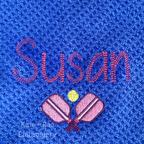 Pickleball Mini Fill Embroidery Design: Crossed pink pickleball paddles below the name Susan in pink on a blue waffle towel