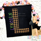 Plaid Embroidery Font: Orange and black plaid letter L with the name LYNCOLN in green and purple on a black shirt
