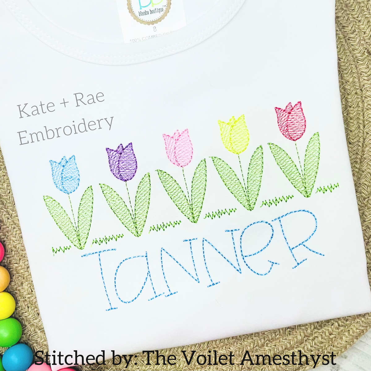 Tulip Garden Sketch Stitch Embroidery Design: Row of five pastel sketch stitch tulips above the name Tanner in blue on a white shirt