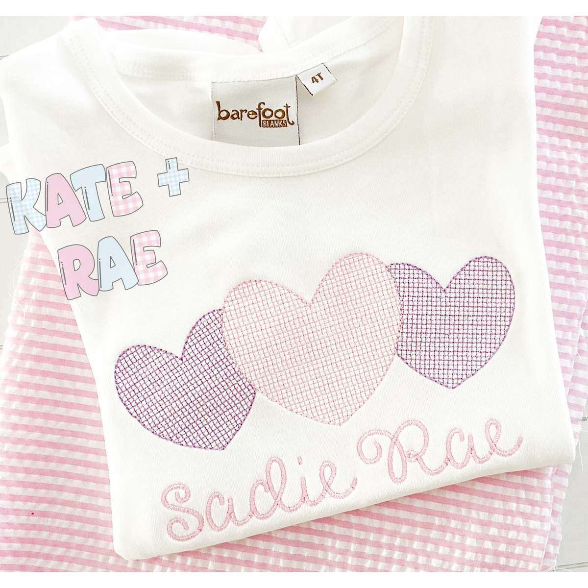 Heart Trio Motif Fill Stitch Embroidery Design: Three motif fill hearts in purple and pink above the name Sadie Rae on a white shirt over pink seersucker