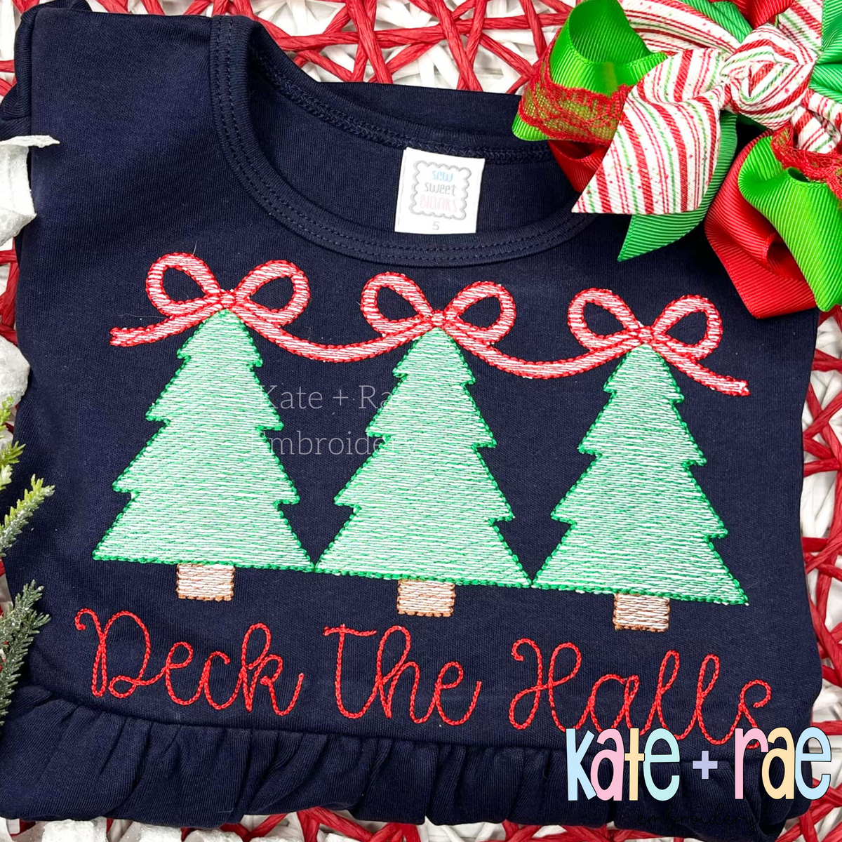 Girls Christmas Tree Trio with Connecting Bows Sketch Stitch Embroidery Design: Three mint Christmas trees linked by pink bows above the words Deck the Halls in red script on a navy shirt