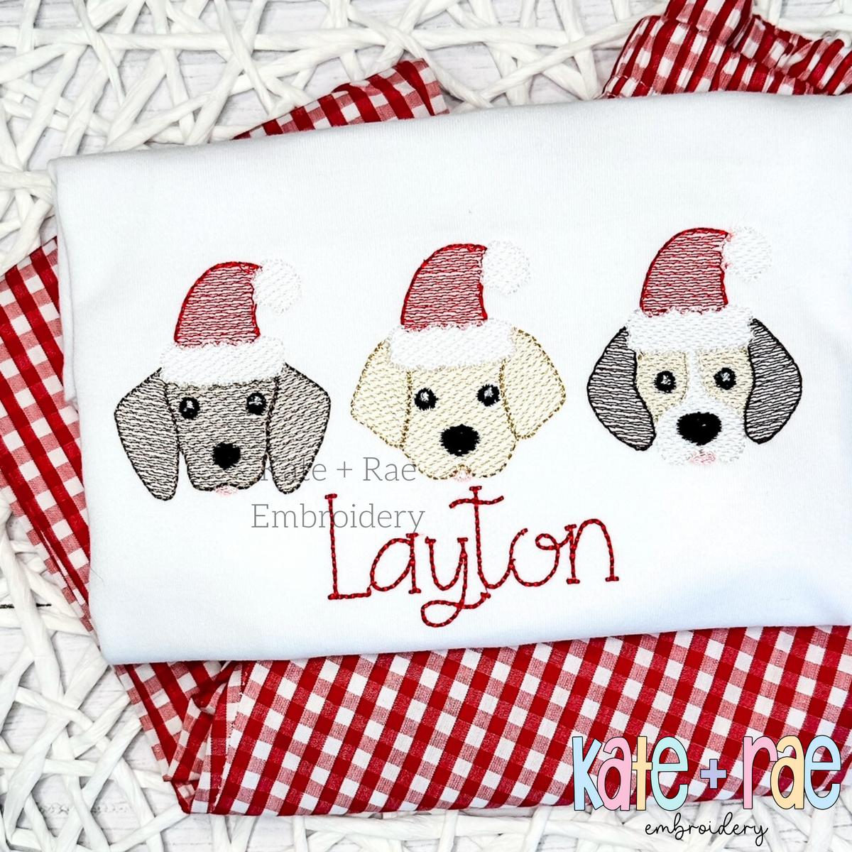 Santa Puppy Trio Sketch Stitch Embroidery Design: Three puppy faces wearing Santa hats above the name Layton in red script on a white shirt