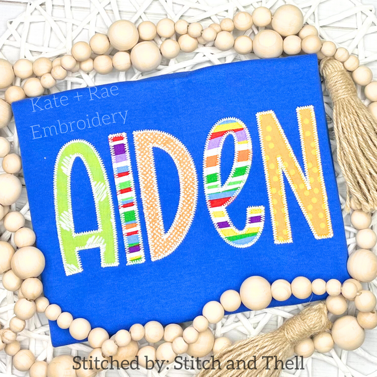 Kinley Zigzag Stitch Applique Embroidery Font: The name Aiden in colorful striped and patterned applique letters on a royal blue shirt
