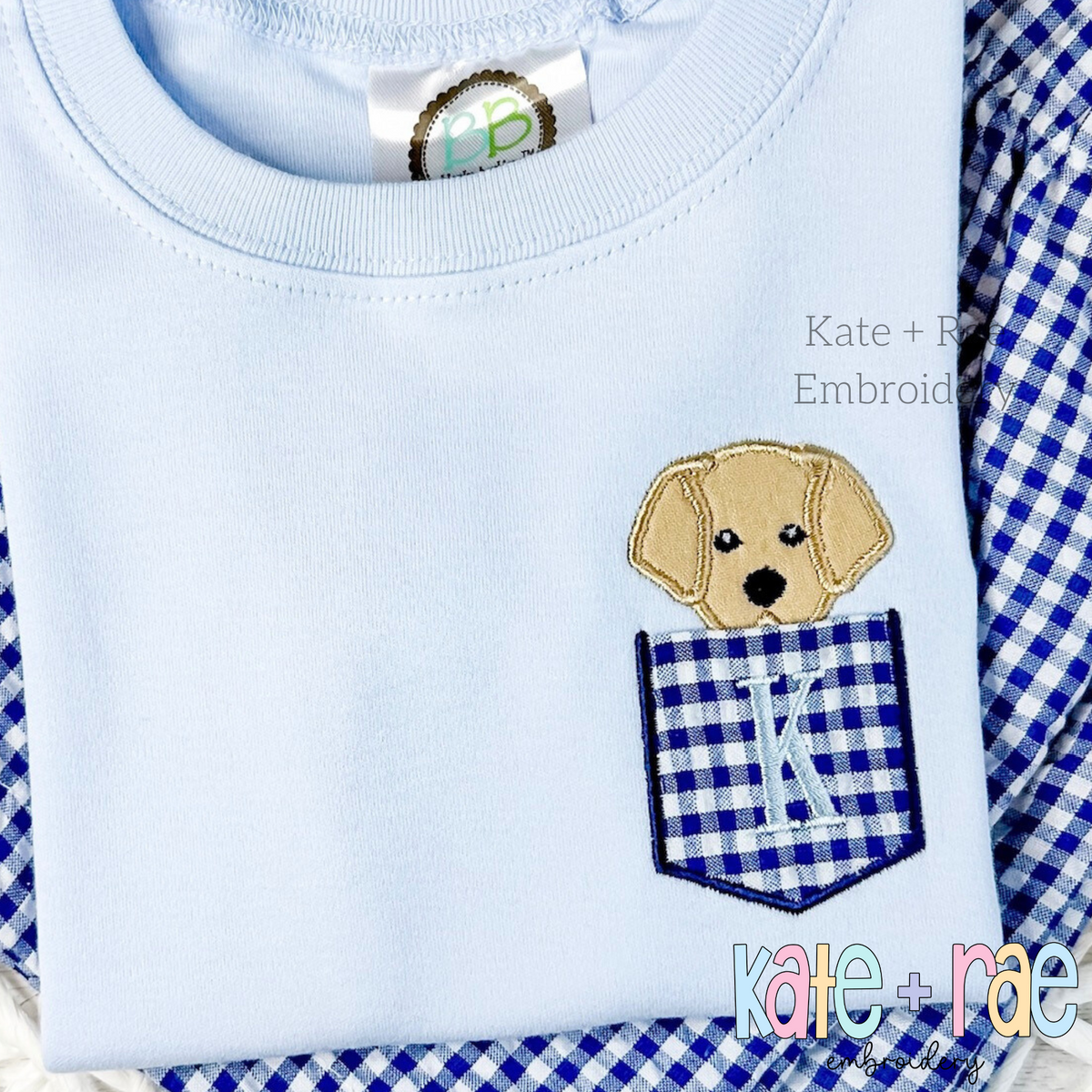 Puppy Dog Pocket Peeper Applique Embroidery Design: Yellow puppy peeking out of a navy gingham pocket with a monogram K on a light blue shirt