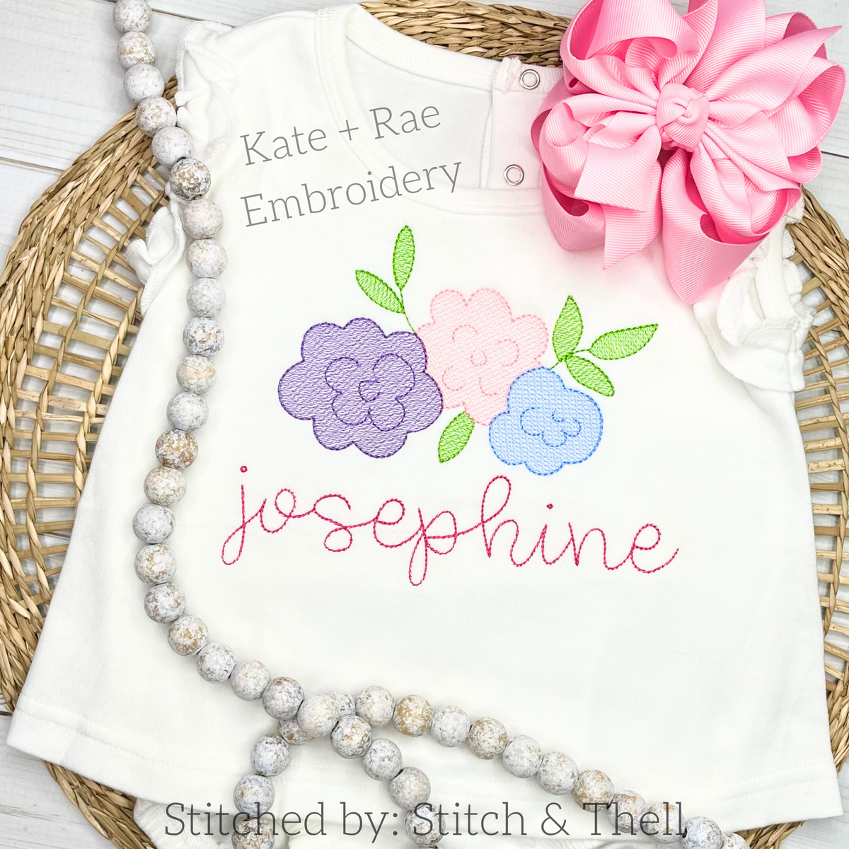 Hello Secret Stitch Embroidery Font: Pastel flowers above the name josephine in pink script on a white shirt with a pink bow