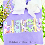 Cupcake Bean Stitch Applique Embroidery Font: The name blakely in pastel floral and gingham applique letters on a purple shirt with a white bow
