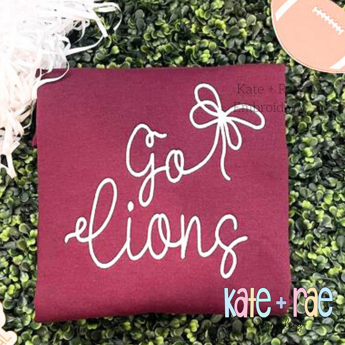 Preppy Go Lions Embroidery Design: The words Go Lions in white script with a white bow on a maroon shirt