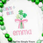 Shamrock Bouquet Mini Fill Embroidery Design: Shamrock bouquet with a pink bow above the name emma in pink on a white shirt