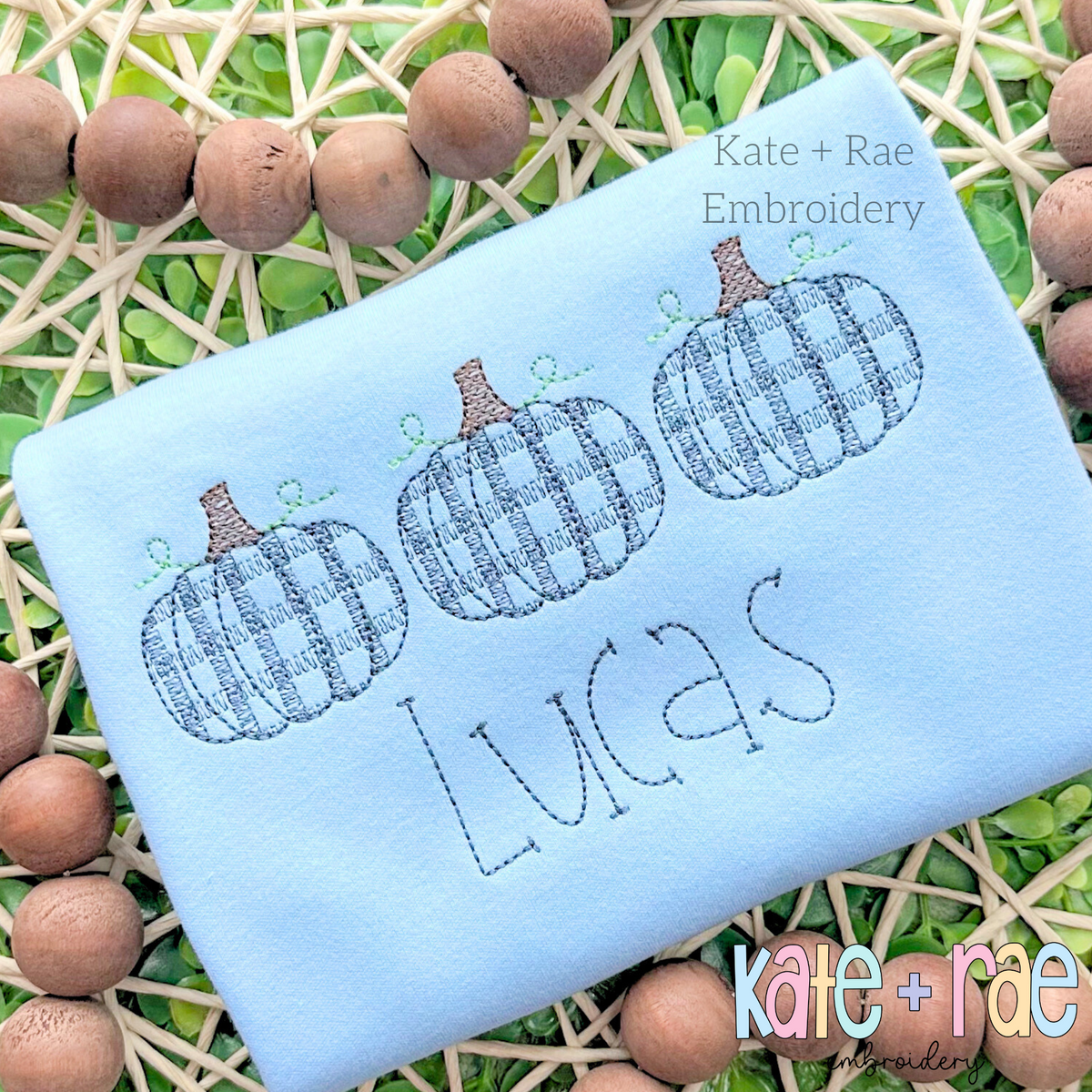 Boy's Plaid Filled Pumpkin Trio Sketch Embroidery Design: Three blue plaid sketch stitch pumpkins above the name Lucas on a light blue shirt