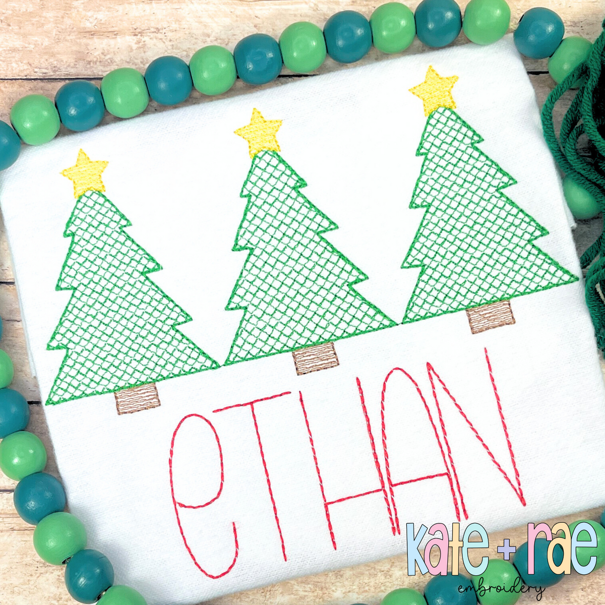Boys Cross Stitch Christmas Tree Trio Sketch Stitch Embroidery Design: Three green cross stitch Christmas trees with yellow stars above the name ETHAN in red on a white shirt