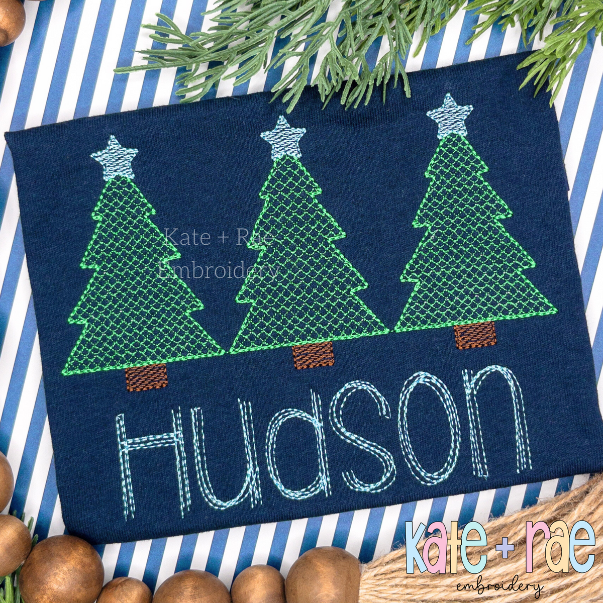 Boys Cross Stitch Christmas Tree Trio Sketch Stitch Embroidery Design: Three green cross stitch Christmas trees with blue stars above the name Hudson on a navy shirt