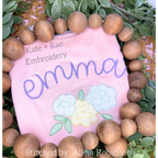 Kinley Floral Sketch Stitch Embroidery Design: The name emma in purple script above pastel sketch stitch flowers on a pink shirt