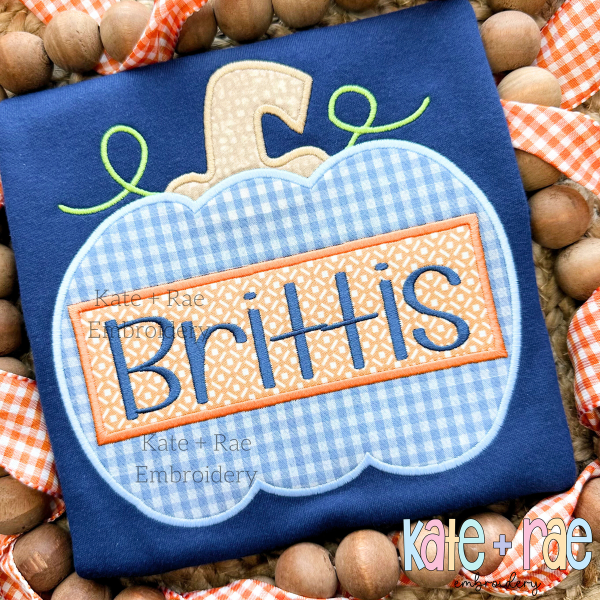 Boy's Pumpkin Satin Applique Embroidery Design: Blue gingham pumpkin applique with a name plate reading Brittis on a navy shirt