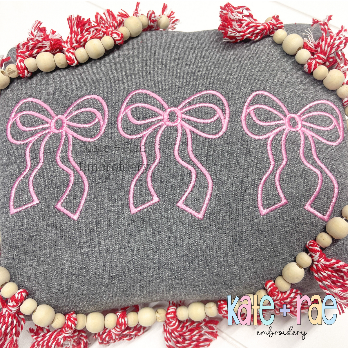 Merritt Bow Trio Satin Stitch Applique Embroidery Design: Three pink outline Merritt bows on a gray sweatshirt