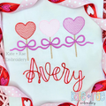 Heart Sucker Trio with Bows Sketch Stitch Embroidery Design: Three heart suckers in red, pink, and purple tied with purple bows above the name Avery in red script on a white shirt