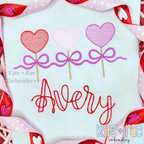 Heart Sucker Trio with Bows Sketch Stitch Embroidery Design: Three heart suckers in red, pink, and purple tied with purple bows above the name Avery in red script on a white shirt