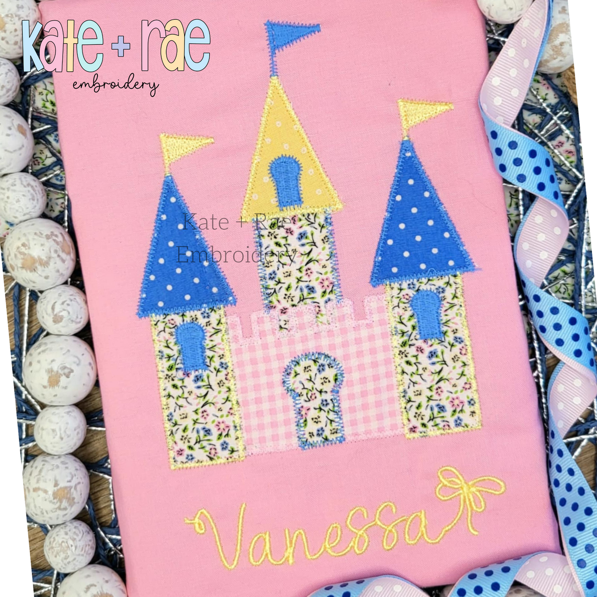Princess Castle Zigzag Stitch Applique Embroidery Design: Princess castle applique with blue polka dot towers and yellow gingham above the name Vanessa in gold script on a pink shirt