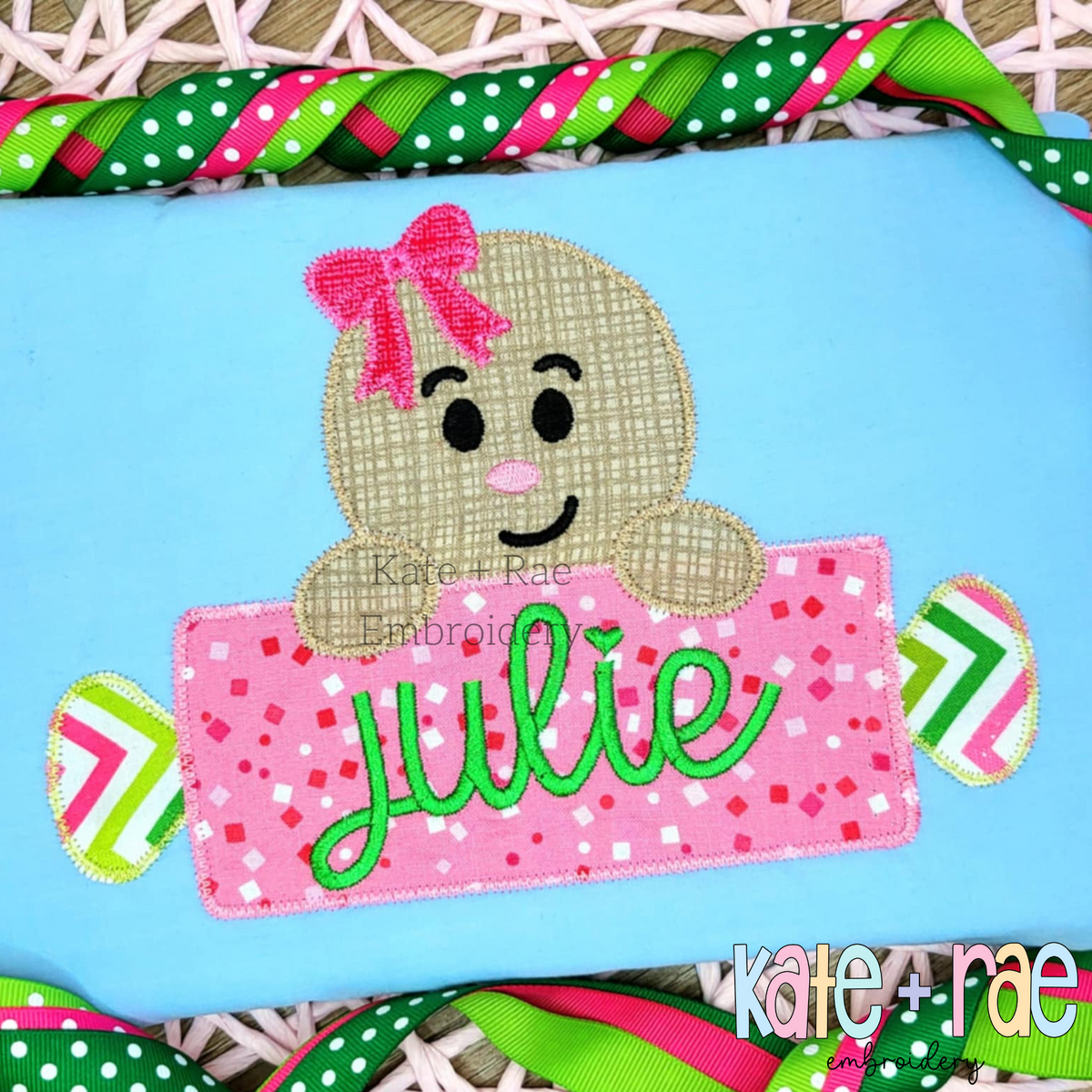 Gingerbread Girl with Rolling Pin Name Plate Zigzag Applique Embroidery Design: Gingerbread girl with a pink bow holding a candy shaped name plate reading julie on a light blue shirt