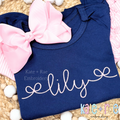 Bow Font Add On Embroidery Design: The name lily in pink script with curly bow ends on a navy shirt