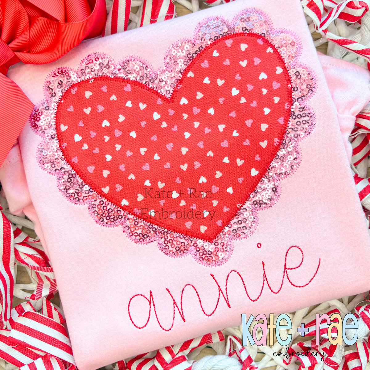 Scalloped Double Heart Zigzag Stitch Applique Embroidery Design: Red heart print applique with a pink sequin scalloped edge above the name annie in pink on a pink shirt