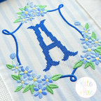 Daisy Floral Crest Satin Stitch Embroidery Design: Blue daisy floral crest around a blue cross stitch letter A on striped fabric