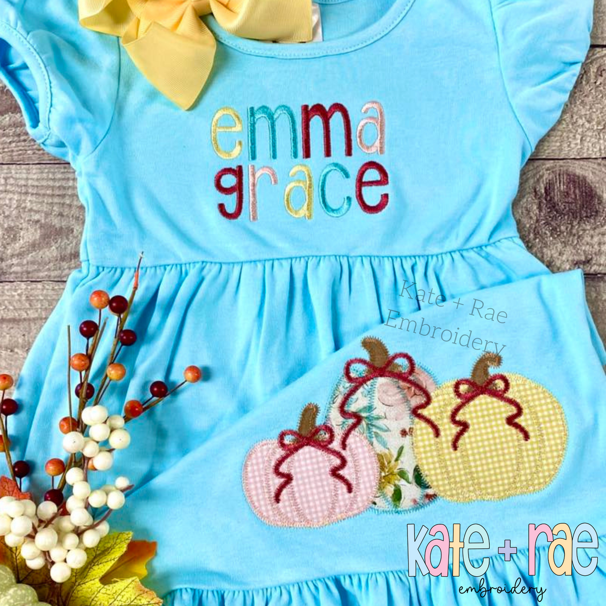Girl's Fall Pumpkin Trio with Bows Zigzag Stitch Applique Machine Embroidery Design: Small pumpkin appliques with bows on the skirt of an aqua dress with emma grace on the front