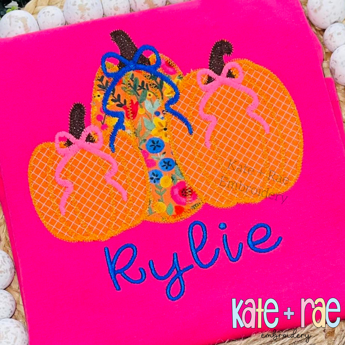 Girl's Fall Pumpkin Trio with Bows Zigzag Stitch Applique Machine Embroidery Design: Orange and floral pumpkin appliques with pink and navy bows above the name Rylie on a hot pink shirt
