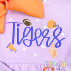 Daisy Handwritten Satin Stitch Embroidery Font: Tigers in blue handwritten satin script with football icons on a lavender shirt