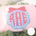 Scallop Circle Monogram Frame with Bow Satin Applique Embroidery Design: Blue gingham scallop circle applique with a pink bow and RAE monogram on a pink shirt
