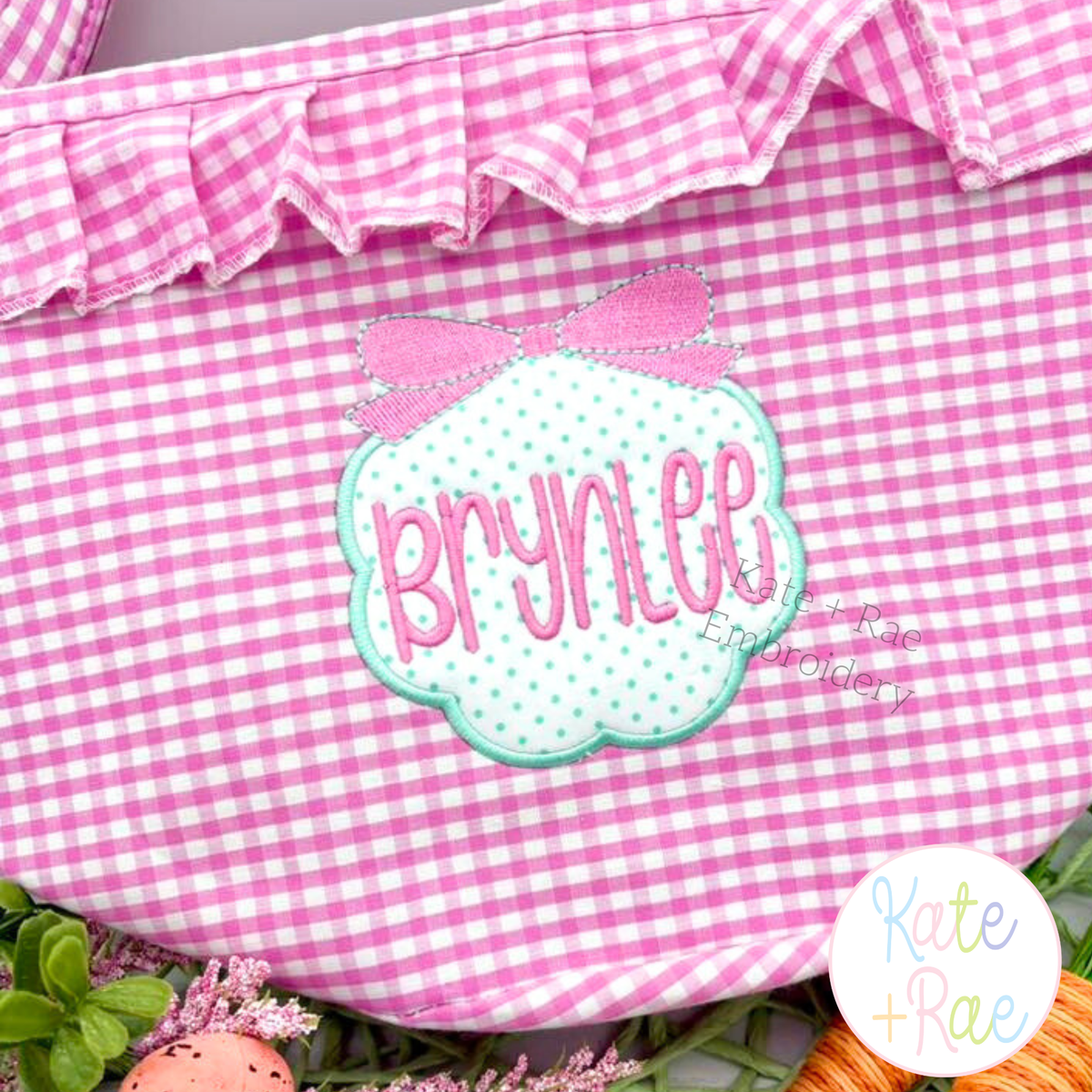 Scallop Circle Monogram Frame with Bow Satin Applique Embroidery Design: Mint scallop frame with a pink bow and the name Brynlee on a pink gingham ruffle bag