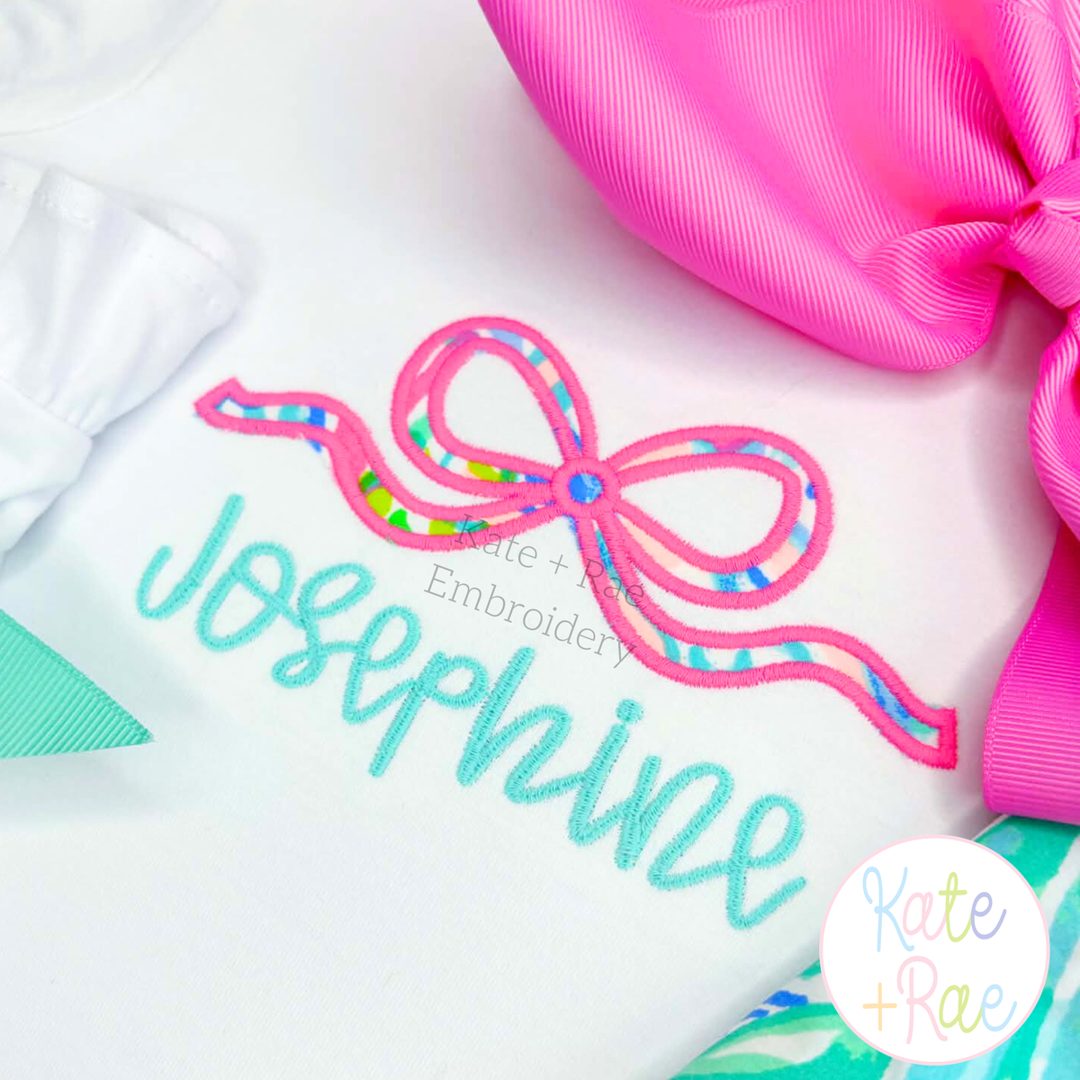 Flowy Longtail Bow Satin Stitch Applique Embroidery Design: Pink and bright print flowy bow satin applique above the name Josephine in aqua script