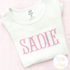 Fishtail Cross Stitch Machine Embroidery Font: The name SADIE in pink fishtail cross stitch letters on a white shirt