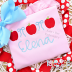 Coquette Apple Fill Stitch Back to School Embroidery Design: Red fill stitch apples with light blue bows above the name Elena in blue script on a pink shirt