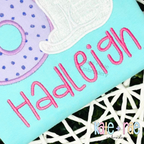 Happy Days Satin Stitch Embroidery Font: The name Hadleigh in pink satin letters beside a purple polka dot applique on an aqua shirt