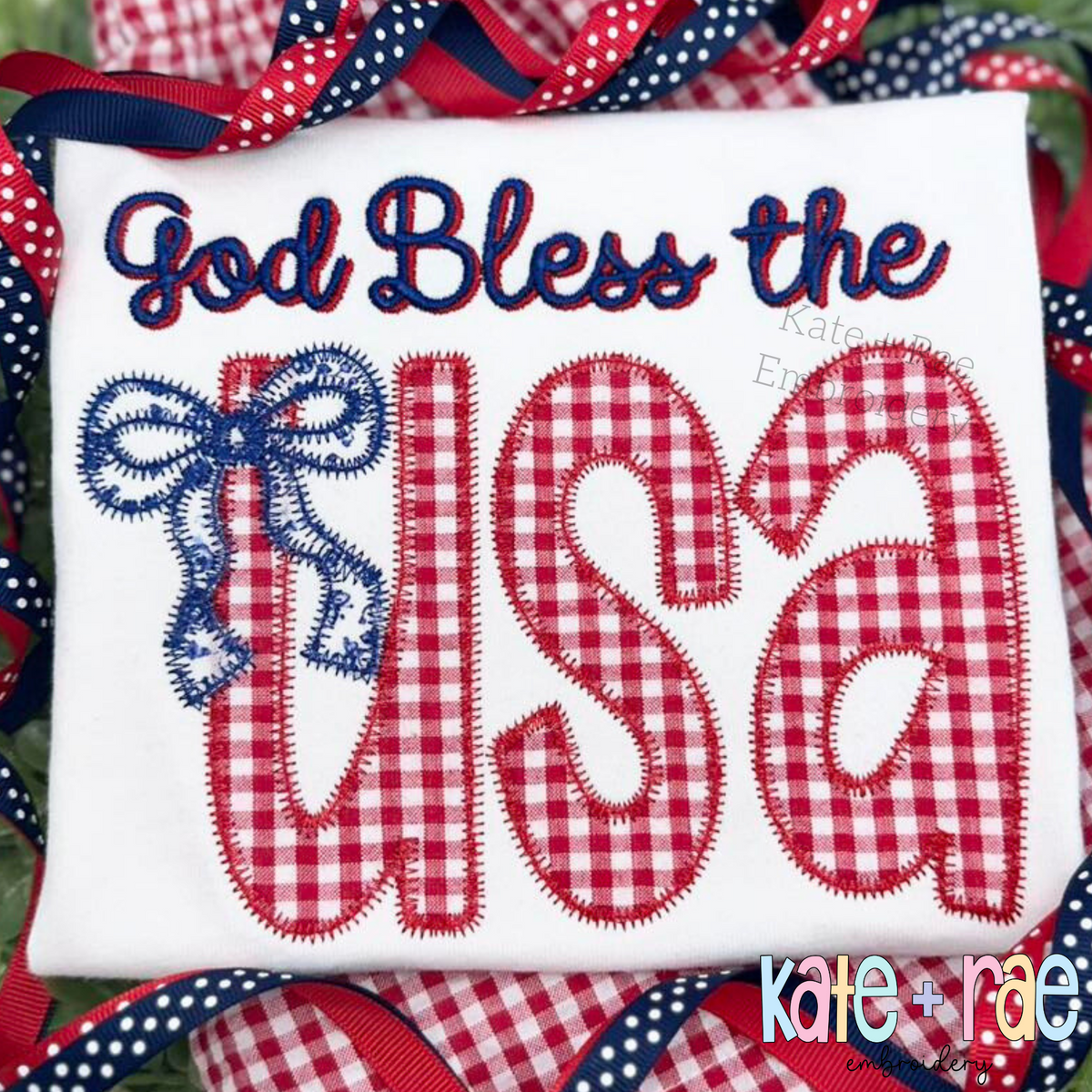 God Bless the USA in navy script and red gingham zigzag applique letters with a blue bow on a white shirt