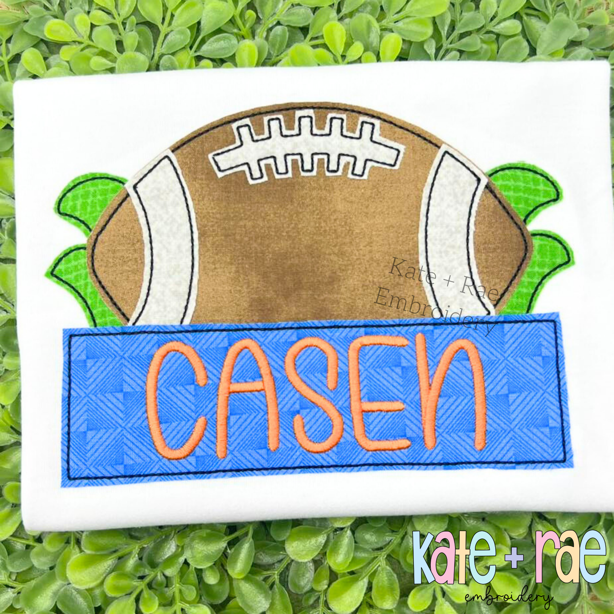 Football with Name Plate Bean Stitch Applique Embroidery Design: Brown football bean applique above a blue name plate reading CASEN in orange on a white shirt