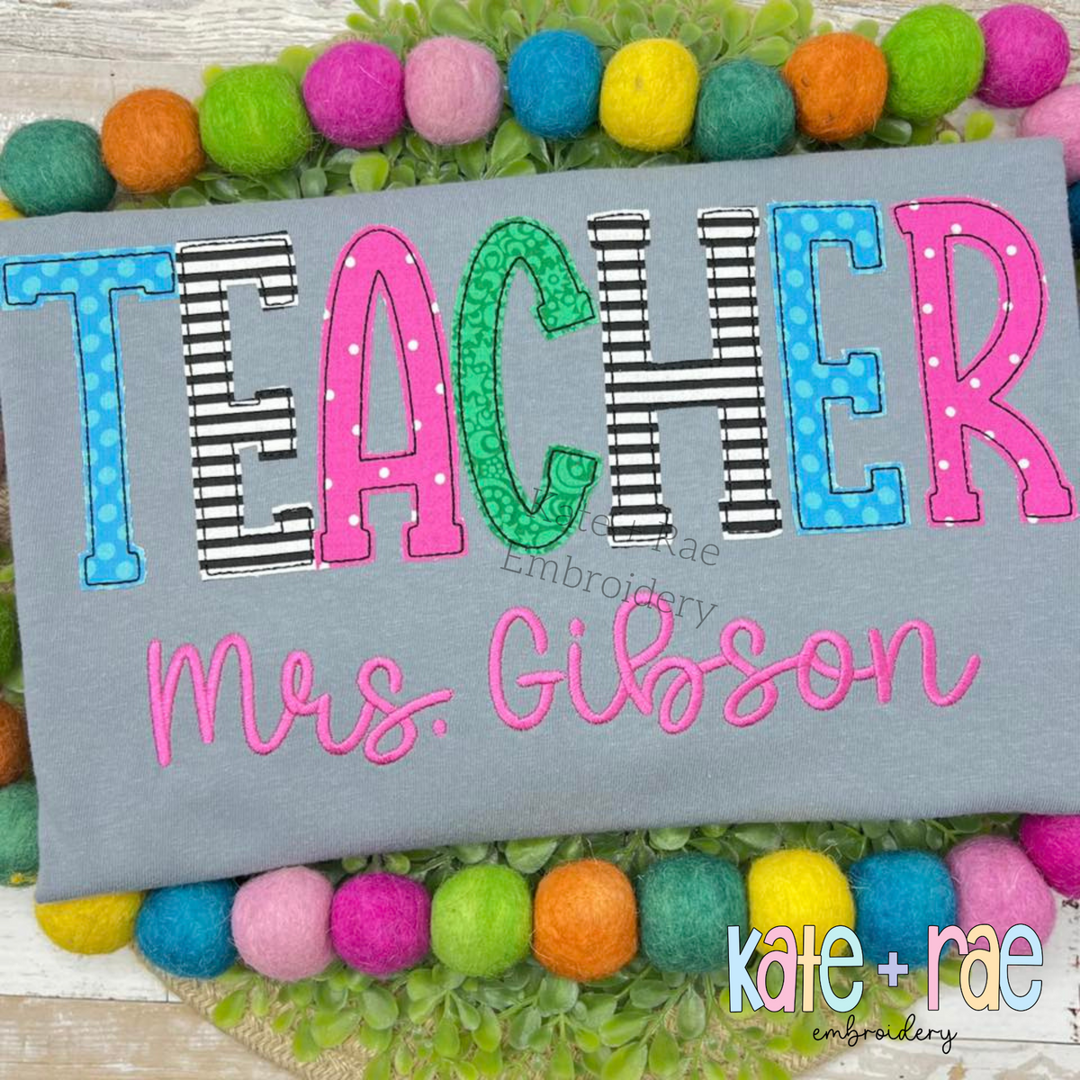 Gracie Bean Stitch Applique Embroidery Font: TEACHER in patterned bean stitch applique letters above Mrs. Gibson in pink script on a gray sweatshirt