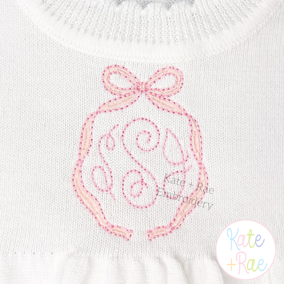 Emma Long Tail Monogram Bow Satin Stitch with Bean Outline Embroidery Design: Pink Emma bow frame with bean outline around a pink script monogram on a white sweater
