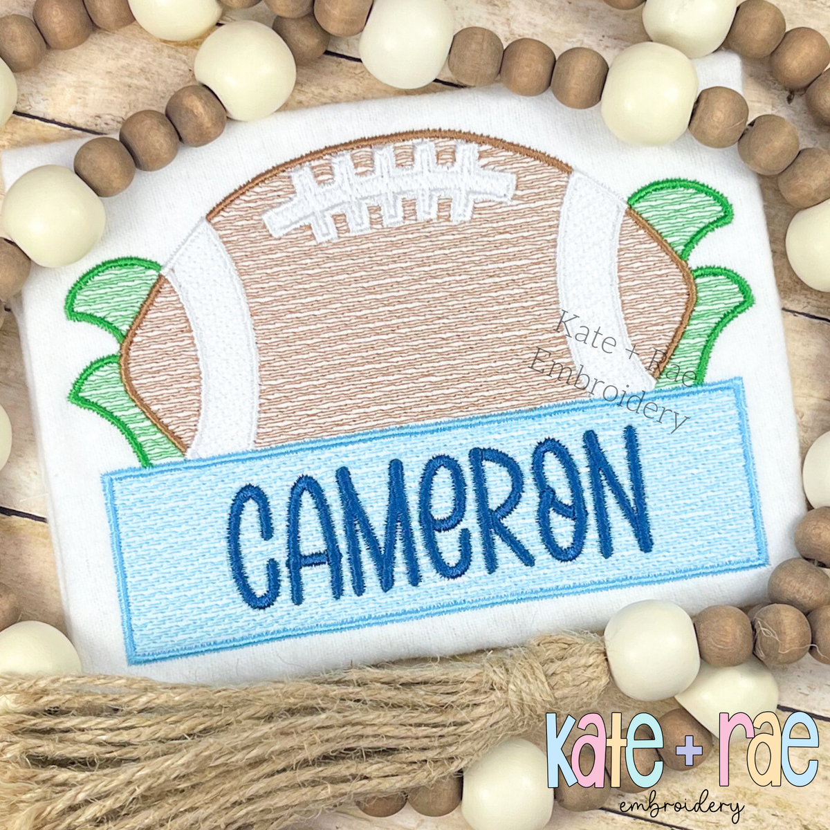 Football with Name Plate Sketch Stitch with Satin Outline Applique Embroidery Design: Sketch football with satin outline above a light blue name plate reading CAMERON in navy
