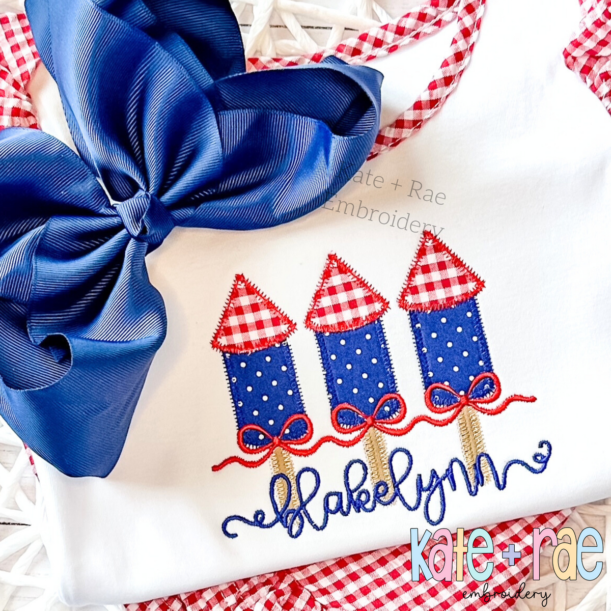 Girl's Firework Trio Zigzag Applique Embroidery Design: Navy polka dot firework appliques with red gingham tops above the name Blakelynn in navy script on a white shirt