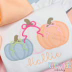 Girl's Fall Pumpkin Trio with Bows Zigzag Stitch Applique Machine Embroidery Design: Blue, pink, and peach pumpkin appliques with bows above the name Hallie in peach script on a white shirt