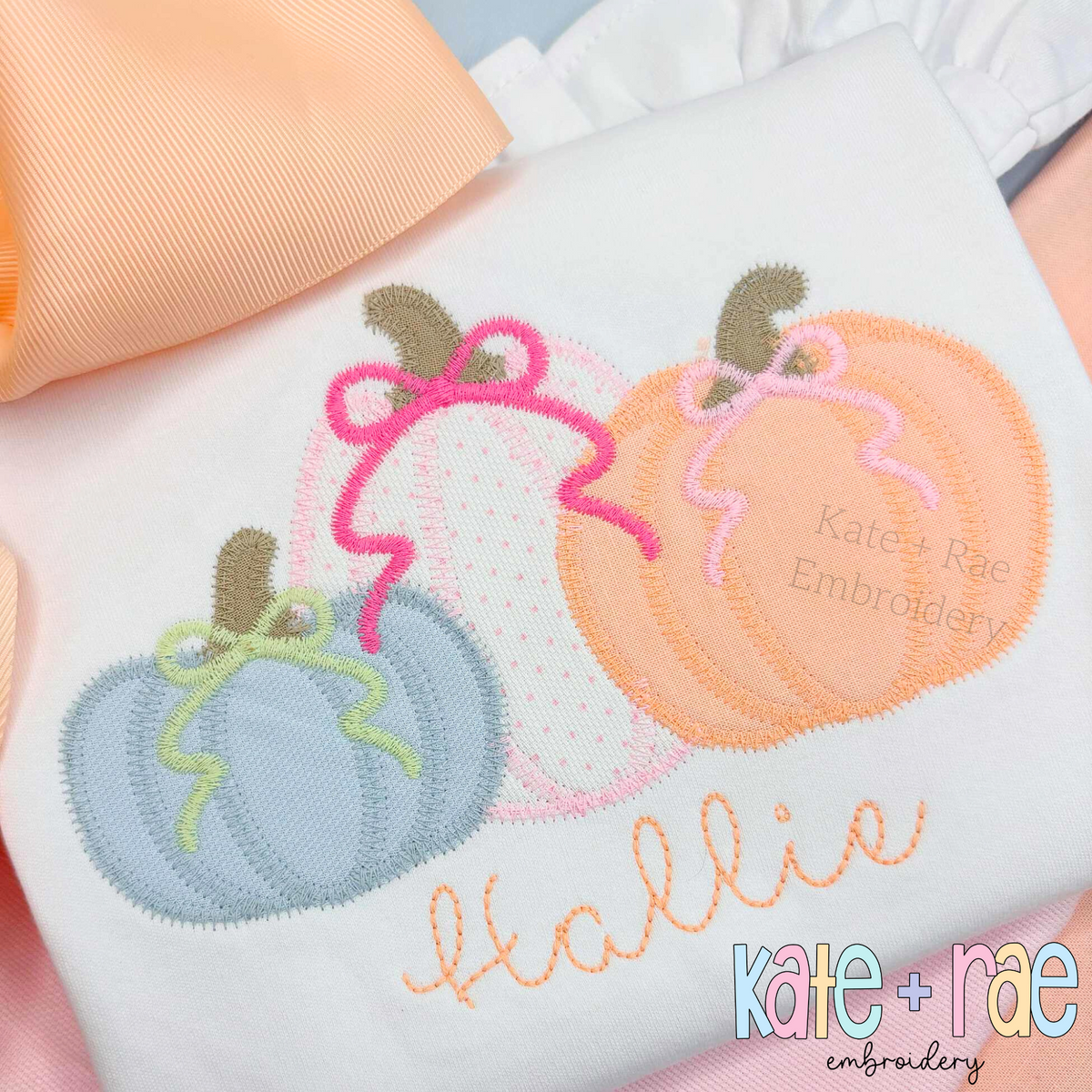 Girl's Fall Pumpkin Trio with Bows Zigzag Stitch Applique Machine Embroidery Design: Blue, pink, and peach pumpkin appliques with bows above the name Hallie in peach script on a white shirt