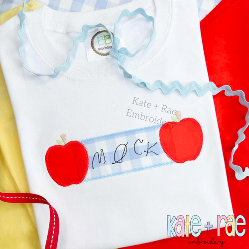 Apple Name Frame Zigzag Applique Embroidery Design: Handwritten name on a blue gingham name plate between two red apple appliques on a white shirt