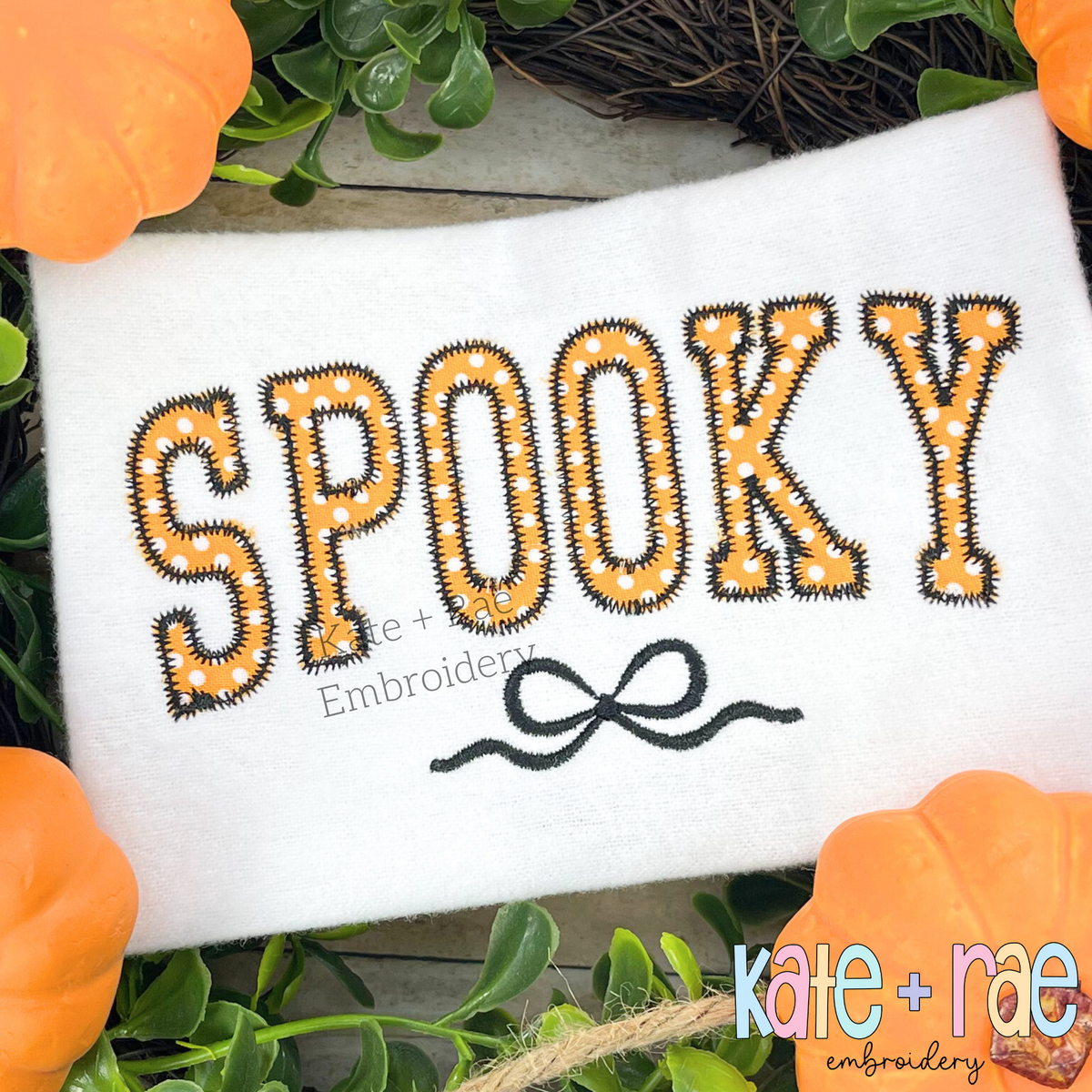 Curved Spooky with Bow Zigzag Stitch Applique Embroidery Design: SPOOKY in orange polka dot zigzag applique letters with a black bow on a white shirt