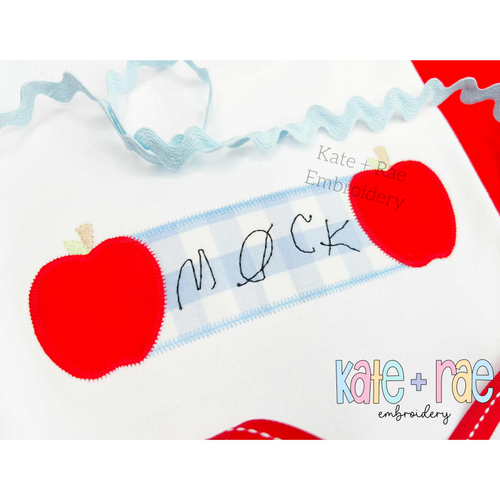 Apple Name Frame Zigzag Applique Embroidery Design: Close-up of red apple appliques on each side of a blue gingham name plate