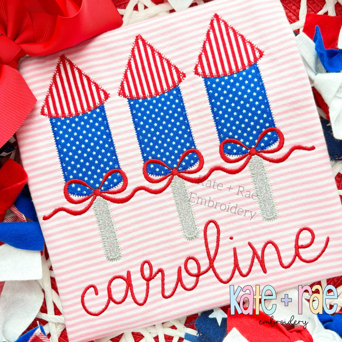 Girl's Firework Trio Zigzag Applique Embroidery Design: Blue polka dot firework appliques with striped tops and red bows above the name caroline on a pink striped shirt